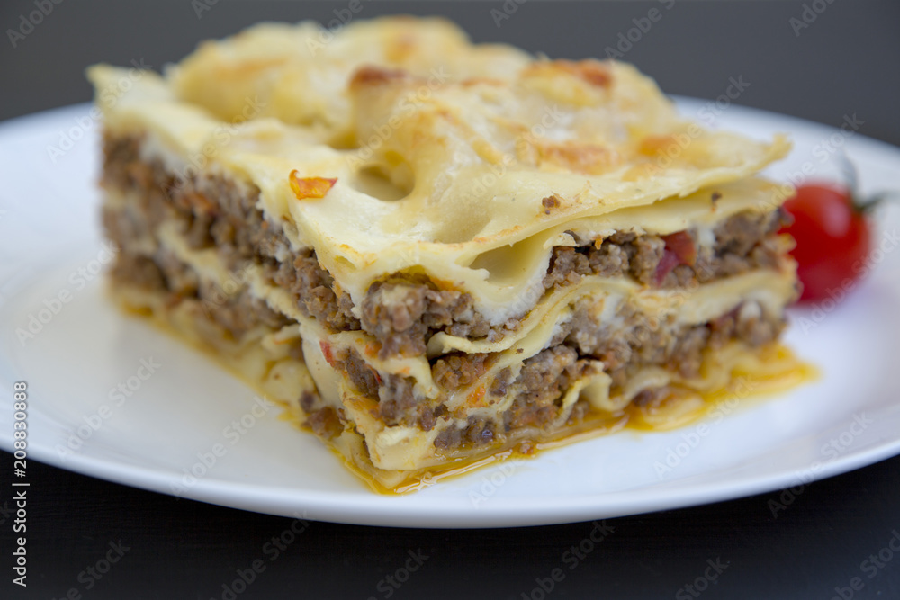 Traditional lasagne on a white plate. Dark background. Side view. Closeup.