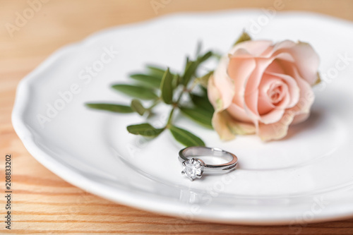 Engagement ring and beautiful rose on plate  closeup