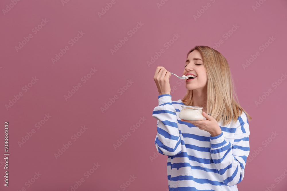 Young attractive woman eating tasty yogurt on color background Young attractive woman eating tasty yogurt on color background