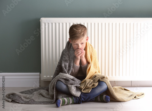 Fotografie Sad little boy suffering from cold on floor near radiator