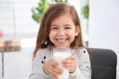 Cute little girl with glass of milk indoors