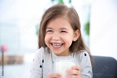 Cute little girl with glass of milk indoors