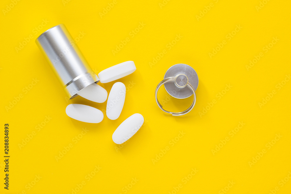 Metal container and pills on a yellow background, close-up