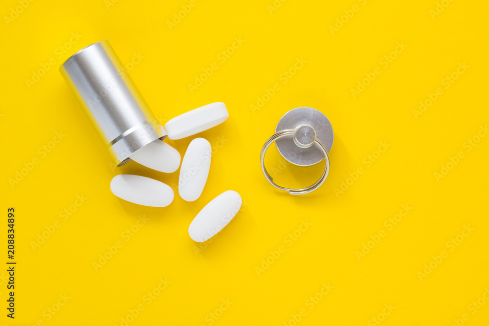 Metal container and pills on a yellow background, close-up Metal container and pills on a yellow background, close-up