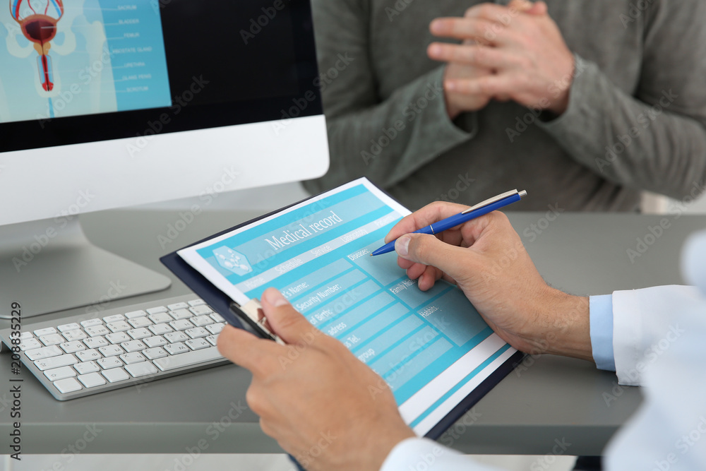 Young urologist filling medical record at table in hospital Young urologist filling medical record at table in hospital