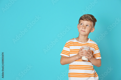 Adorable little boy with glass of milk on color background