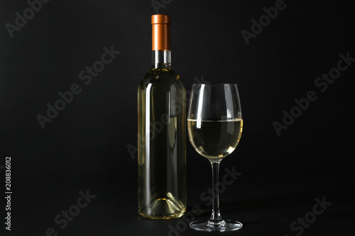 Bottle and glass of expensive white wine on dark background