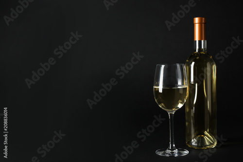 Bottle and glass of expensive white wine on dark background