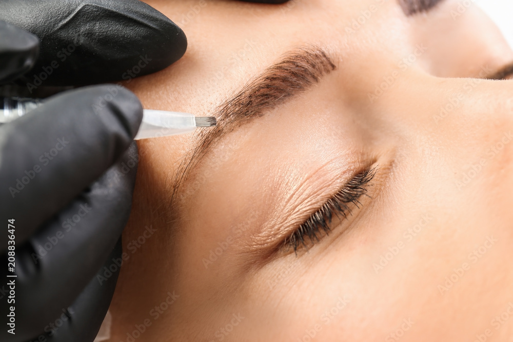 Young woman undergoing eyebrow correction procedure in salon