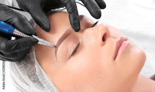 Fotografija Young woman undergoing eyebrow correction procedure in salon