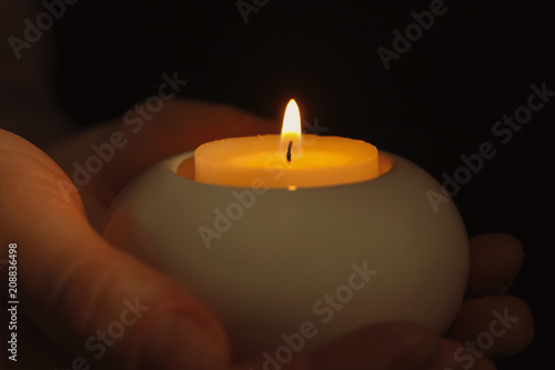 Young person holding burning candle in darkness, closeup