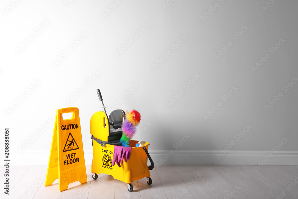 Safety sign with phrase CAUTION WET FLOOR and mop bucket on