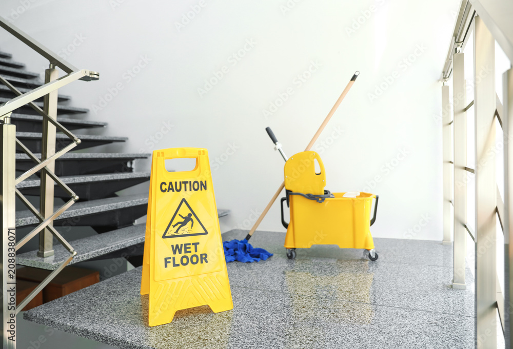 Safety sign with phrase "CAUTION WET FLOOR" and mop bucket on stairs