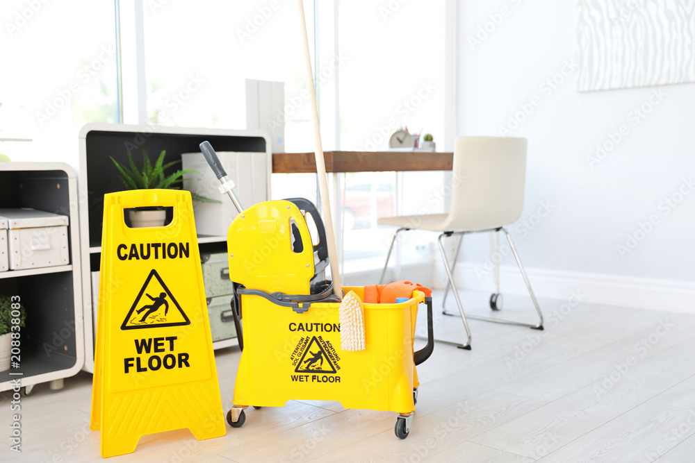 Phrase "CAUTION WET FLOOR" on safety sign and mop bucket with cleaning