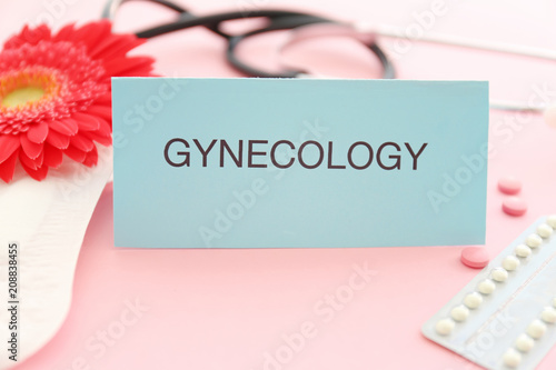 Card with word GYNECOLOGY, menstrual pad and birth control pills on color background