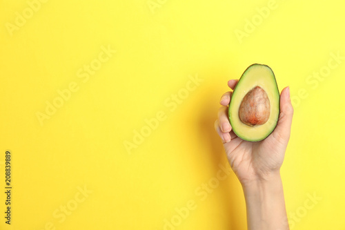 Woman holding ripe cut avocado on color background