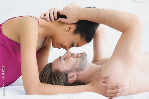 side view of multiethnic young couple in love lying in bed together in morning