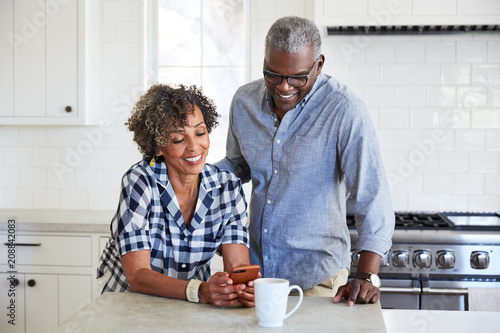 African American Senior Couple looking at cell phone in the kitchen together
