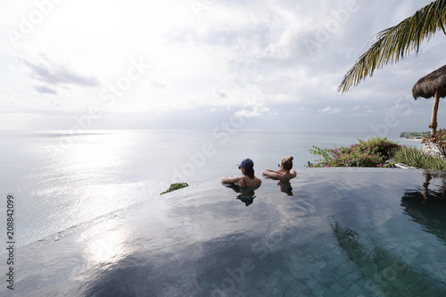 Two young attractive women relaxing in an infinity pool photo