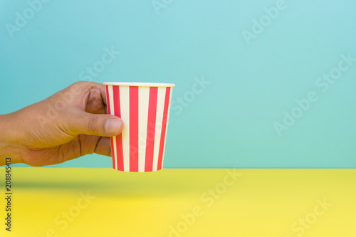 hand holding a colorful party paper cup, yellow and blue background © Krisada