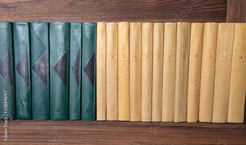 multivolume books of dark green and beige color neatly stacked on a shelf