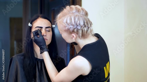 young woman gets eyebrow correction procedure. kosmetolog- makeup artist applies paint with brush on eyebrows in beauty saloon. Professional care for face. photo