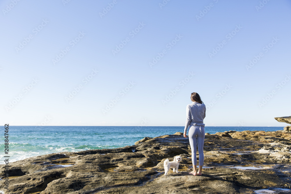 A woman standing with her dog by the ocean A woman standing with her dog by the ocean