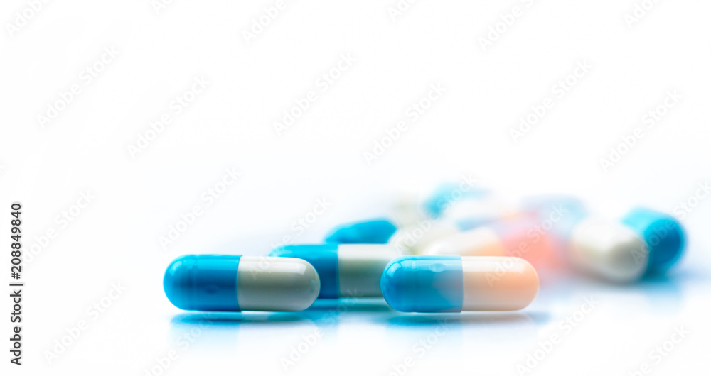 Selective focus on blue and white capsules pill spread on white background with shadow. Global healthcare concept. Antibiotics drug resistance. Antimicrobial capsule pills. Pharmaceutical industry. Selective focus on blue and white capsules pill spread on white background with shadow. Global healthcare concept. Antibiotics drug resistance. Antimicrobial capsule pills. Pharmaceutical industry.