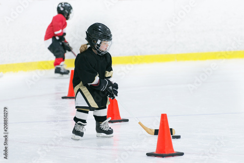Little cute girl is playing hockey on ice wearing in full hockey equipment. She does workouts with a stick and puck. 