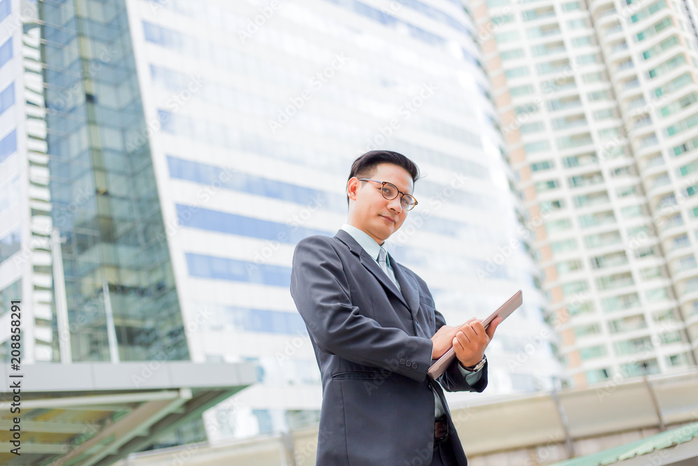 Young Asia businessman in suit with his laptop computer outdoors, modern building on the background Young Asia businessman in suit with his laptop computer outdoors, modern building on the background
