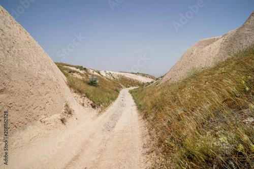 Walking unpaved rough sand trail route through desert mountain grass  landscape of dried ancient red valley with clear sky background  Cappadocia