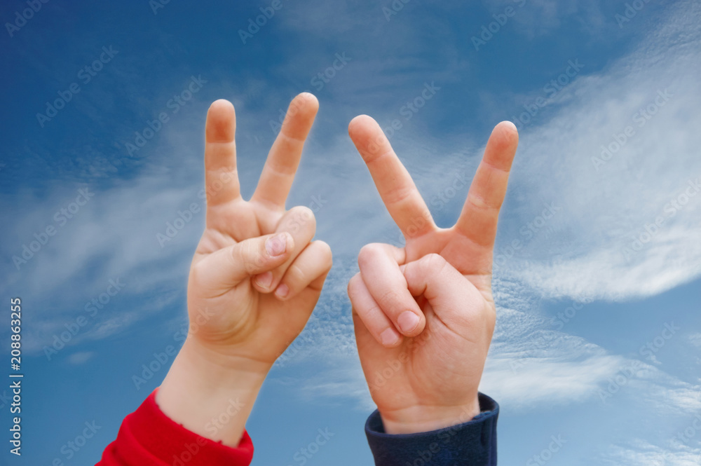 two children's hand displaying peace sign against the blue sky two children's hand displaying peace sign against the blue sky