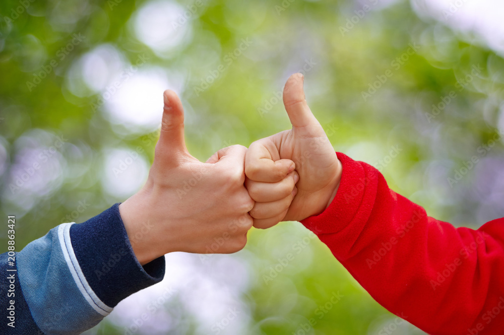 two children's hands thumb upagainst a green natural background