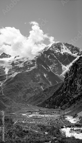 Black and white tall mountain landscape with snow, clouds and hut