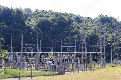 High voltage electric lines cross the hilly mestnost. Electric station in the summer under the open sky. Power industry. Ecology of nature. Metal technological structures. Strategic object at a field.