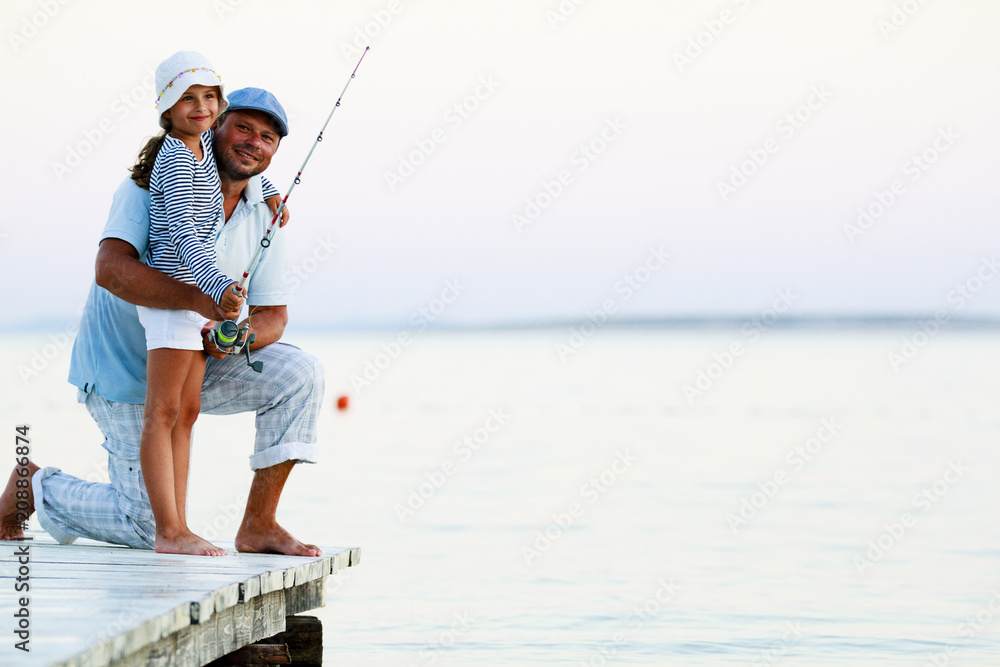 Father with his daughter fishing in a sea on a wood pier at sunset. Father with his daughter fishing in a sea on a wood pier at sunset.