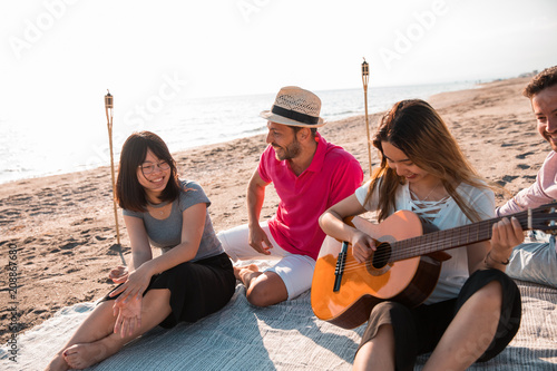 Happy multiracial young people playing guitar and making picnic at the beach. Friends, music and holiday concept. © ManuPadilla