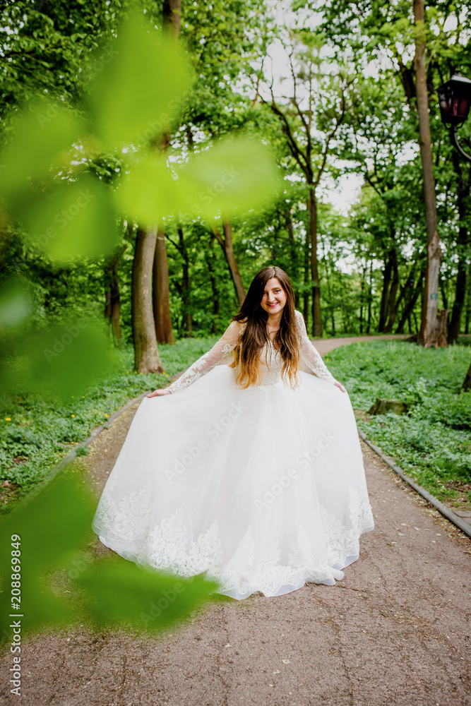 A refined bride in a white dress poses in the park