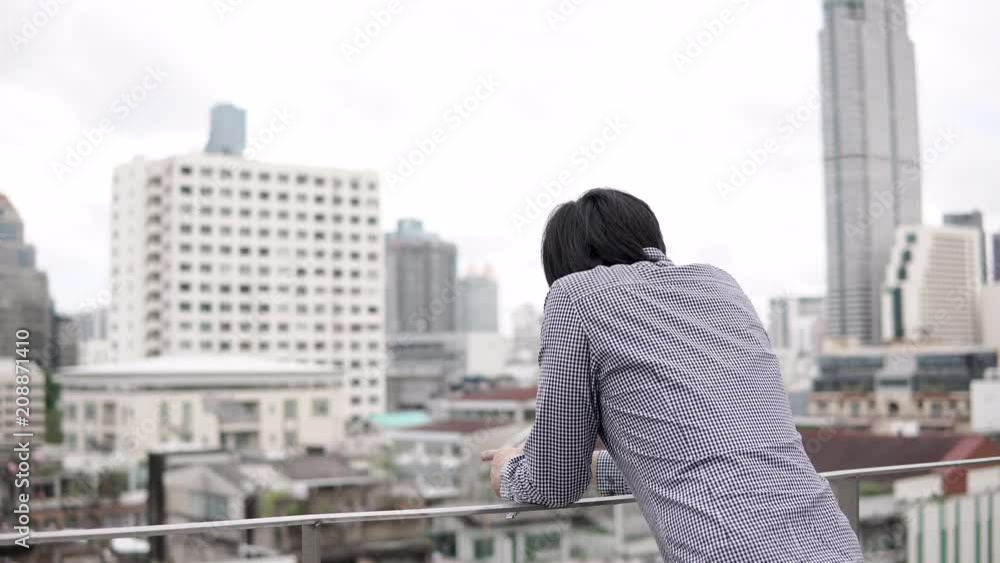 Young Asian businessman standing on office building rooftop terrace looking at city view in the background. Urban lifestyle concepts. 4K video Young Asian businessman standing on office building rooftop terrace looking at city view in the background. Urban lifestyle concepts. 4K video