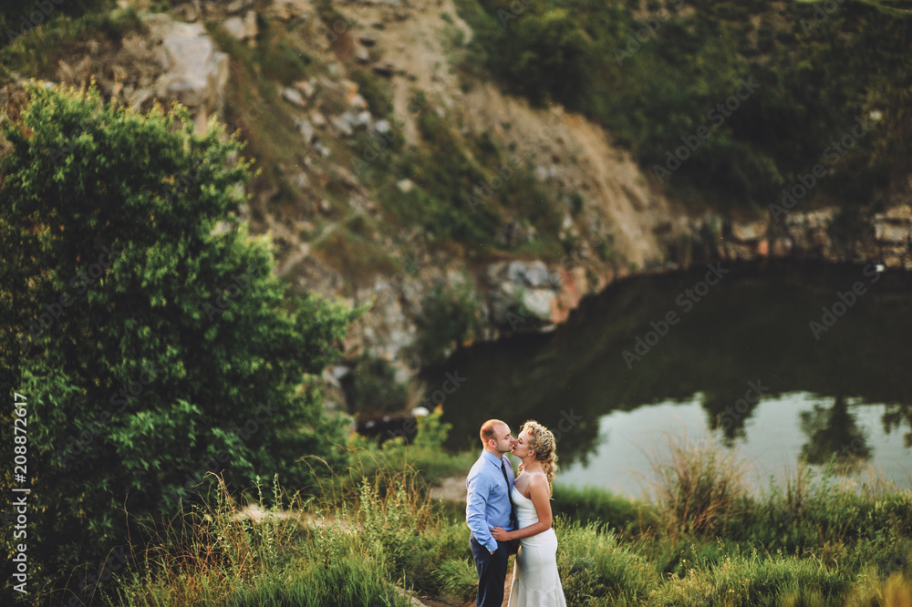 Beautiful and lovely newlyweds stand on a cliff, against the background of rocks and river. Wedding portrait of a stylish bride and a cute bride.