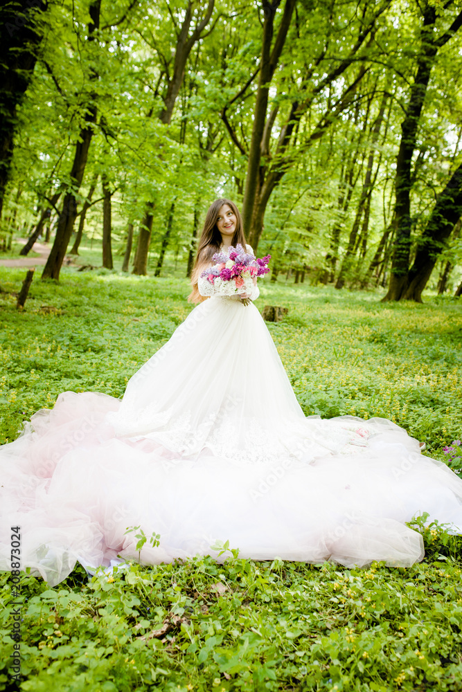 A sweet girl in a white dress is in the park with a bouquet in her hands