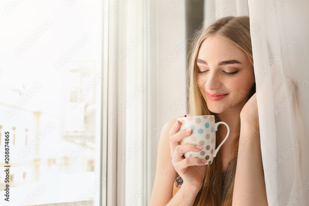 Young woman drinking coffee while standing near window at home Young woman drinking coffee while standing near window at home