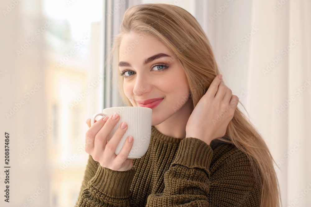 Young woman drinking coffee while standing near window at home Young woman drinking coffee while standing near window at home