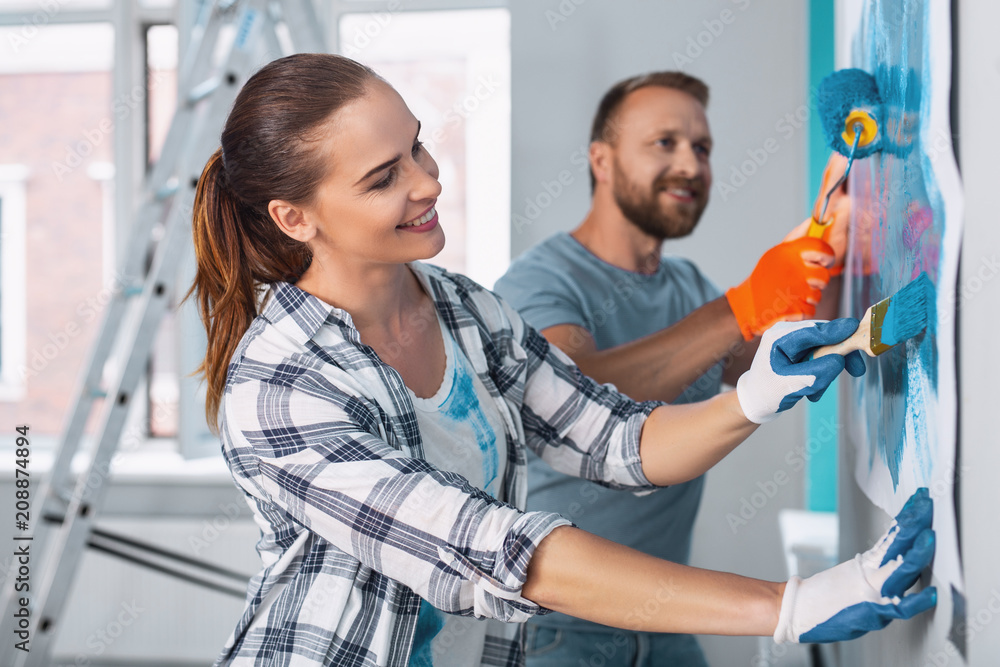 Our work. Inspired dark-haired painter painting the wall and working with her colleague Our work. Inspired dark-haired painter painting the wall and working with her colleague