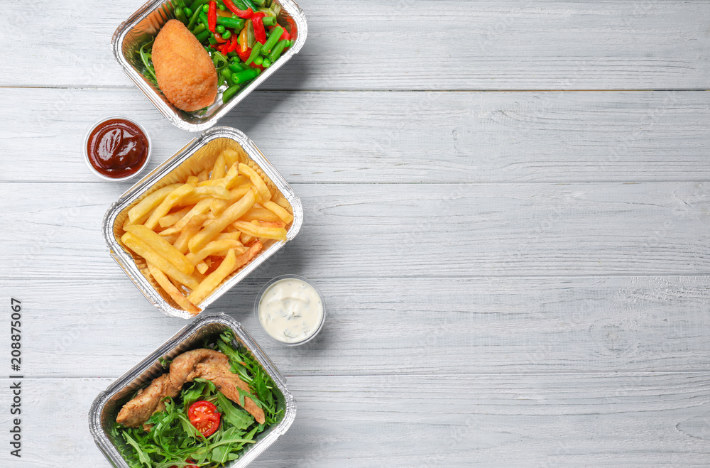 Foil containers with delicious food on wooden background
