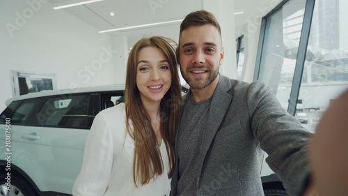 Point of view shot of young couple have online vidoe call in car dealership after purchasing car. Man is holding camera and woman is showing keys, they are talking and kissing. photo