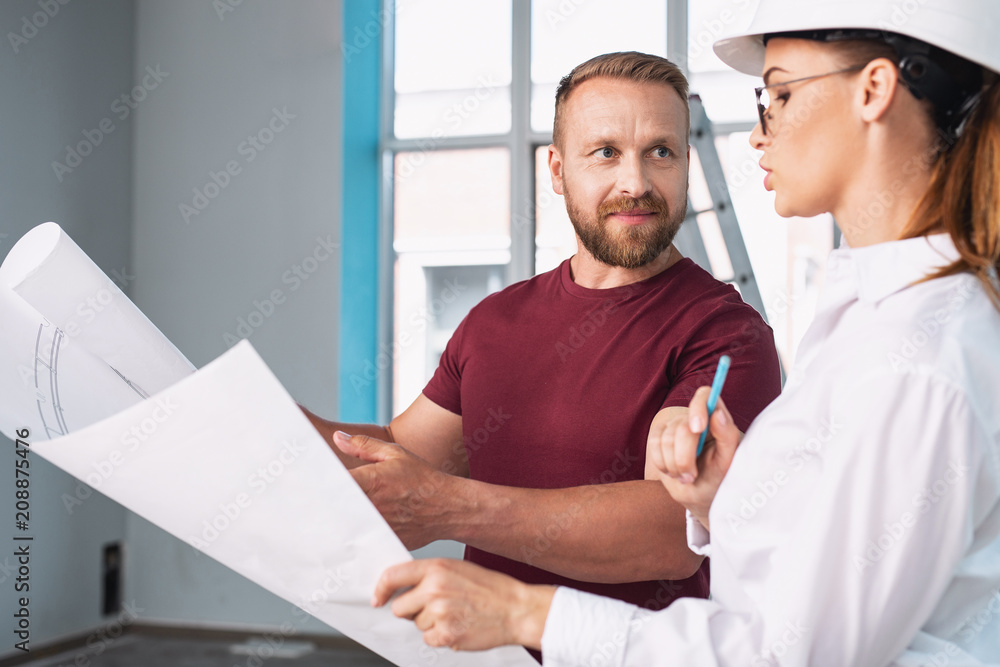 Discussing the project. Handsome well-built man holding a sketch and discussing it with his designer Discussing the project. Handsome well-built man holding a sketch and discussing it with his designer