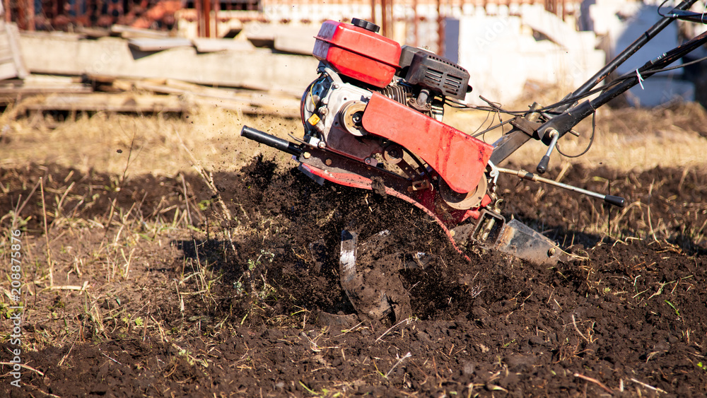 Worker with a machine cultivator digs the soil in the garden Worker with a machine cultivator digs the soil in the garden