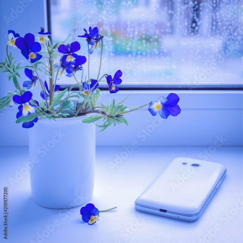 Bouquet of wildflowers and a mobile phone on the windowsill. Blue flowers pansies. Toned image.