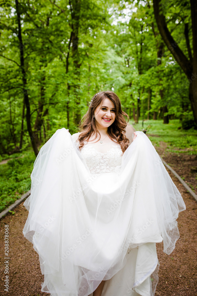 An graceful girl in a white dress walks along the path in the park